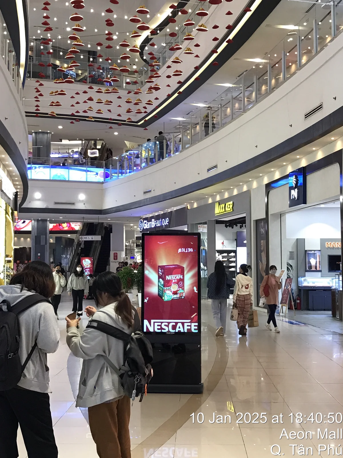 Shoppers passing a digital advertising display at AEON Mall Tân Phú